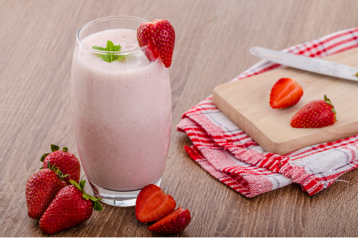 A glass with strawberry and fyogur smoothie decorated with a piede of fruit and some mint.