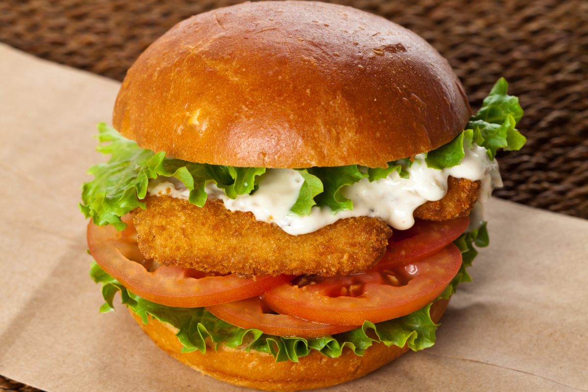 A burger bun with fish sticks, or fish fingers, lettuce, tomato slices and mayonnaise.