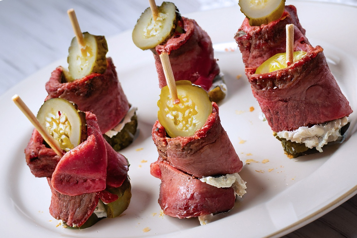 A plate with beef bites, roast beef slices with cream cheese spread rolled around pickles, generative AI.