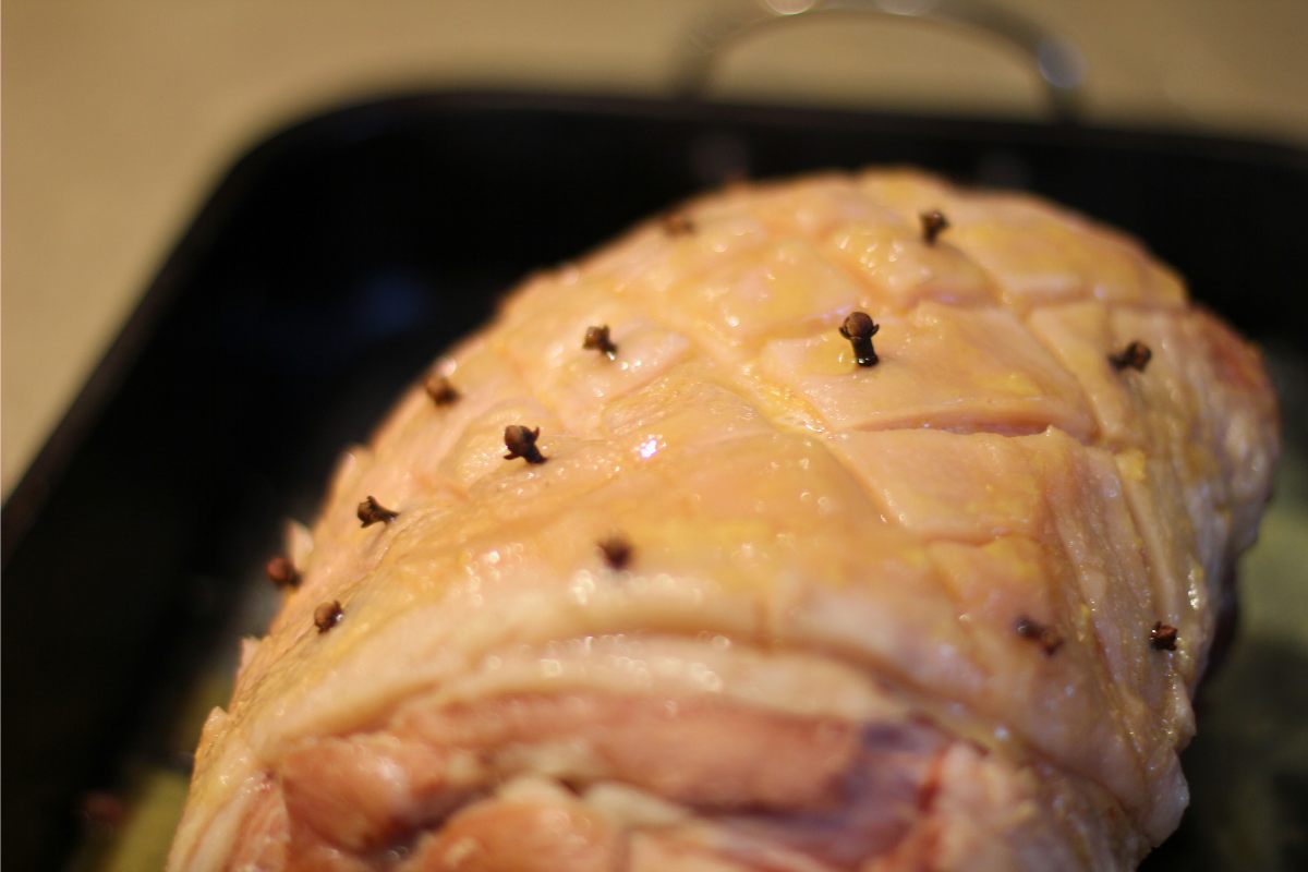 An oven pan with baked ham decorated with cloves.