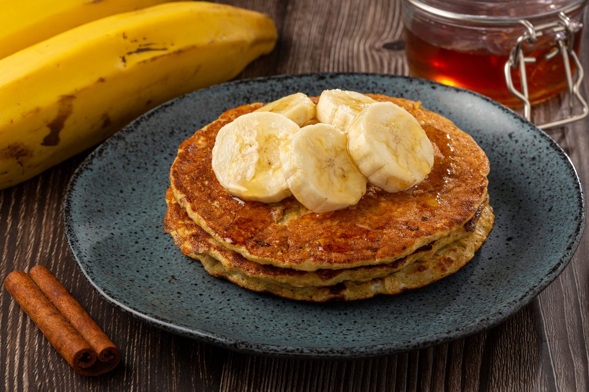 A plate of banana and oat pancakes with honey and banana slices on top.
