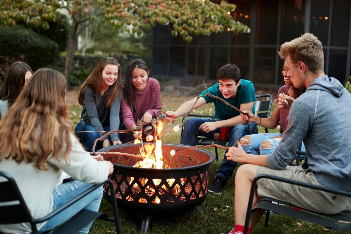 Teens toasting marshmallow around an open fire.