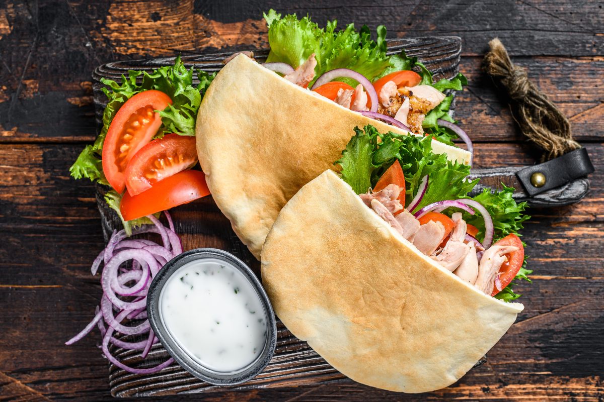 Two pita pockets filled with cooked meat and salad vegetables, served with sauce on the side.