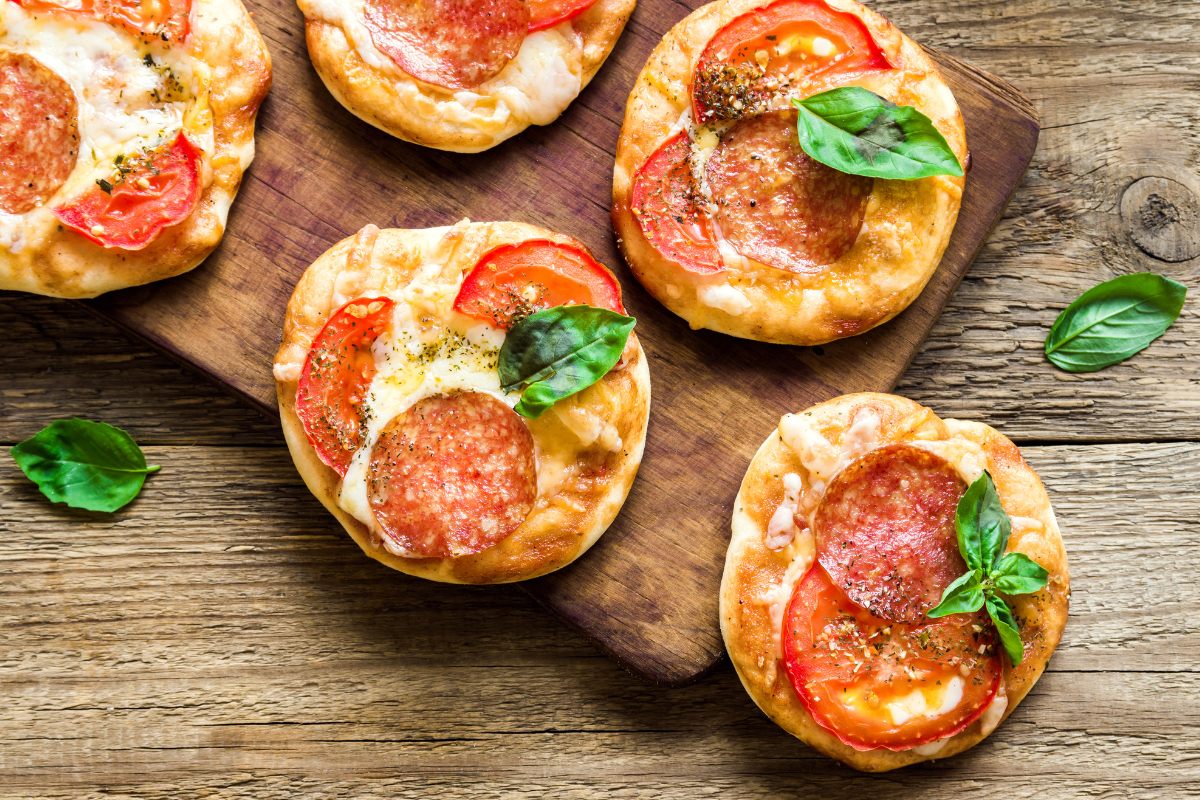 Five individual pepperoni pizzas on a board.