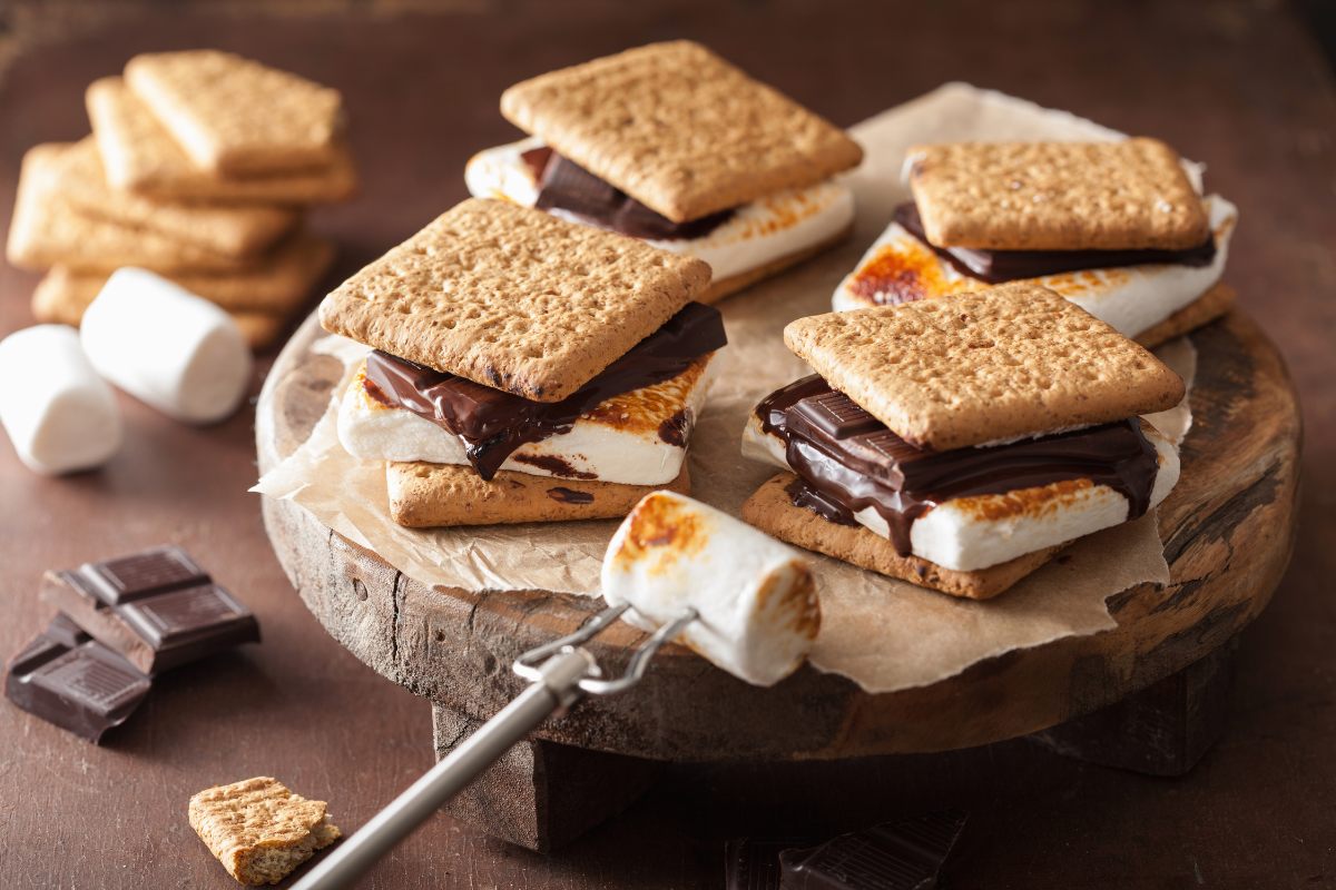 Four home made s'mores on a board and one half-roasted marshmallow in a fork.
