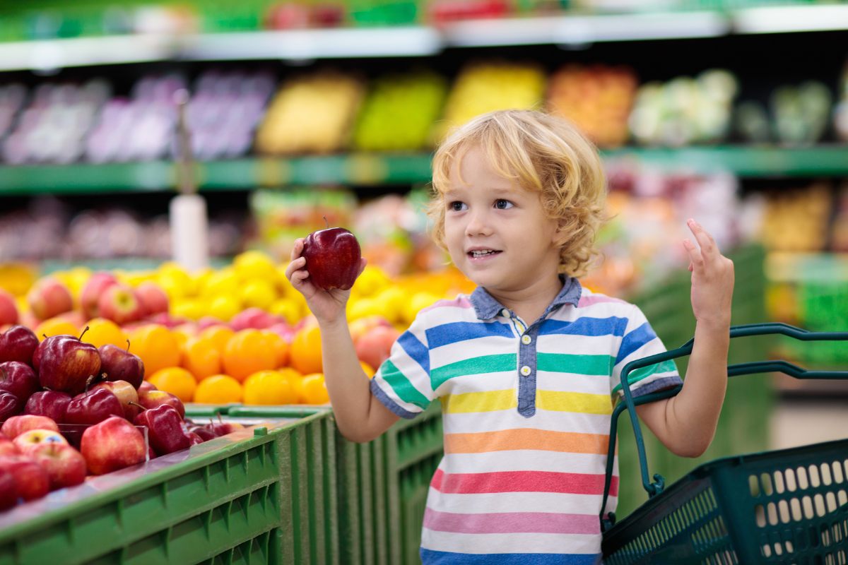 At the supermarket, a little boy holds an apple and he seems to be counting.