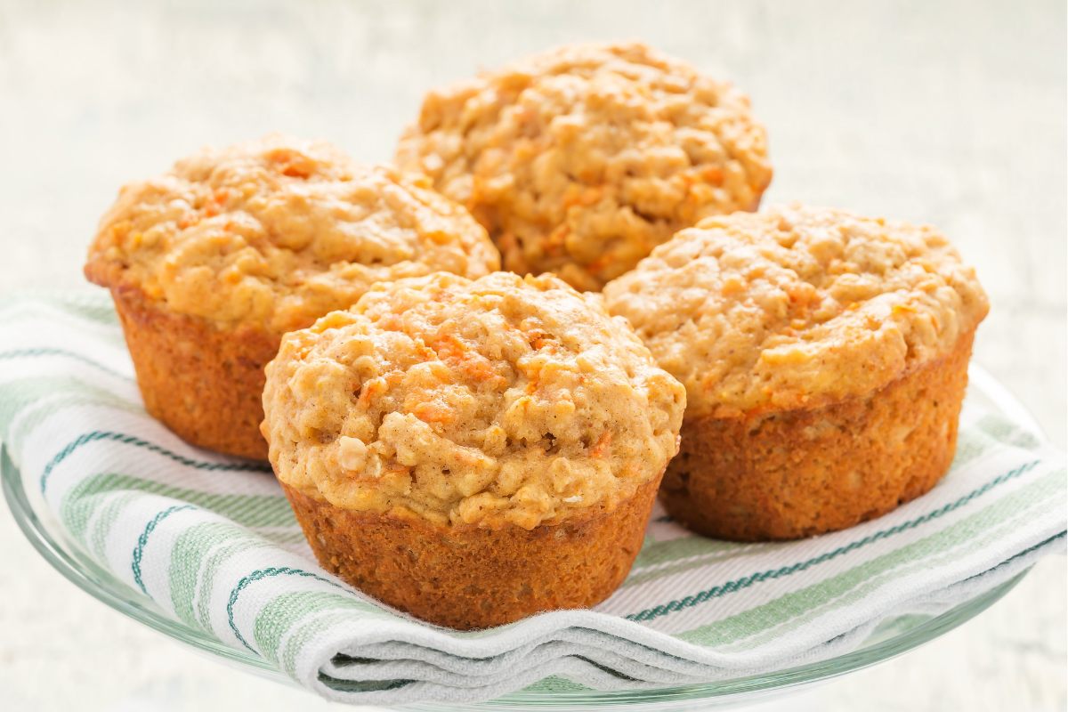 Four carrot muffins on a light green clean kitchen towel.