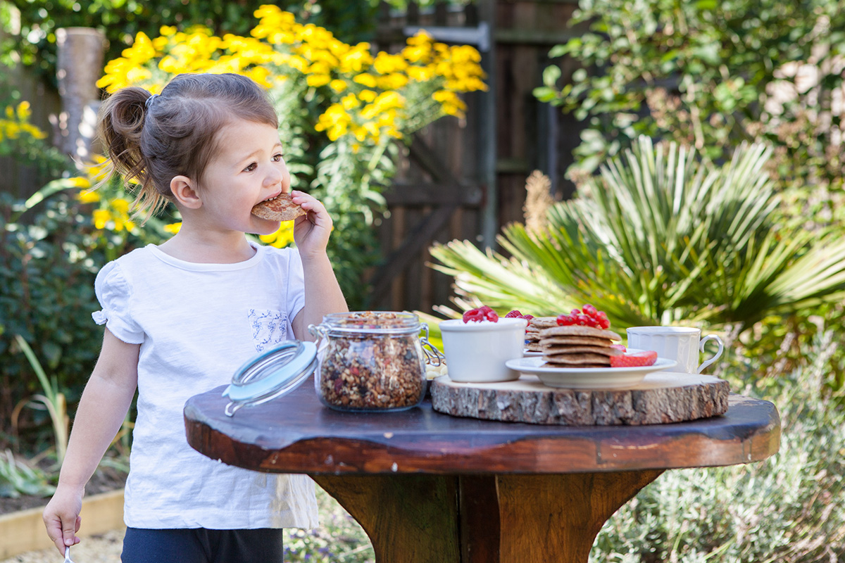 Little girl eating a flourless banana and almond pancake in the garden.