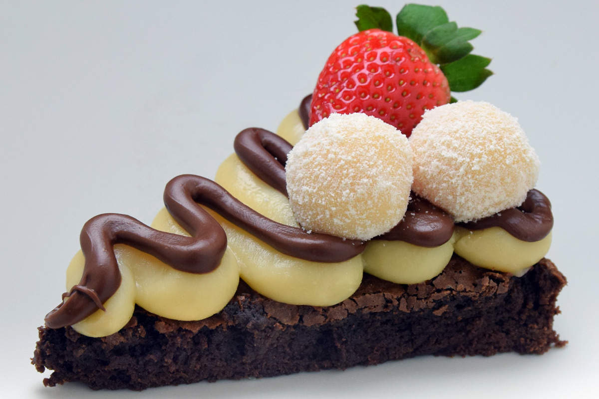 A slice of brownie dessert pizza with decorated with chocolate-hazelnut paste and a strawberry.