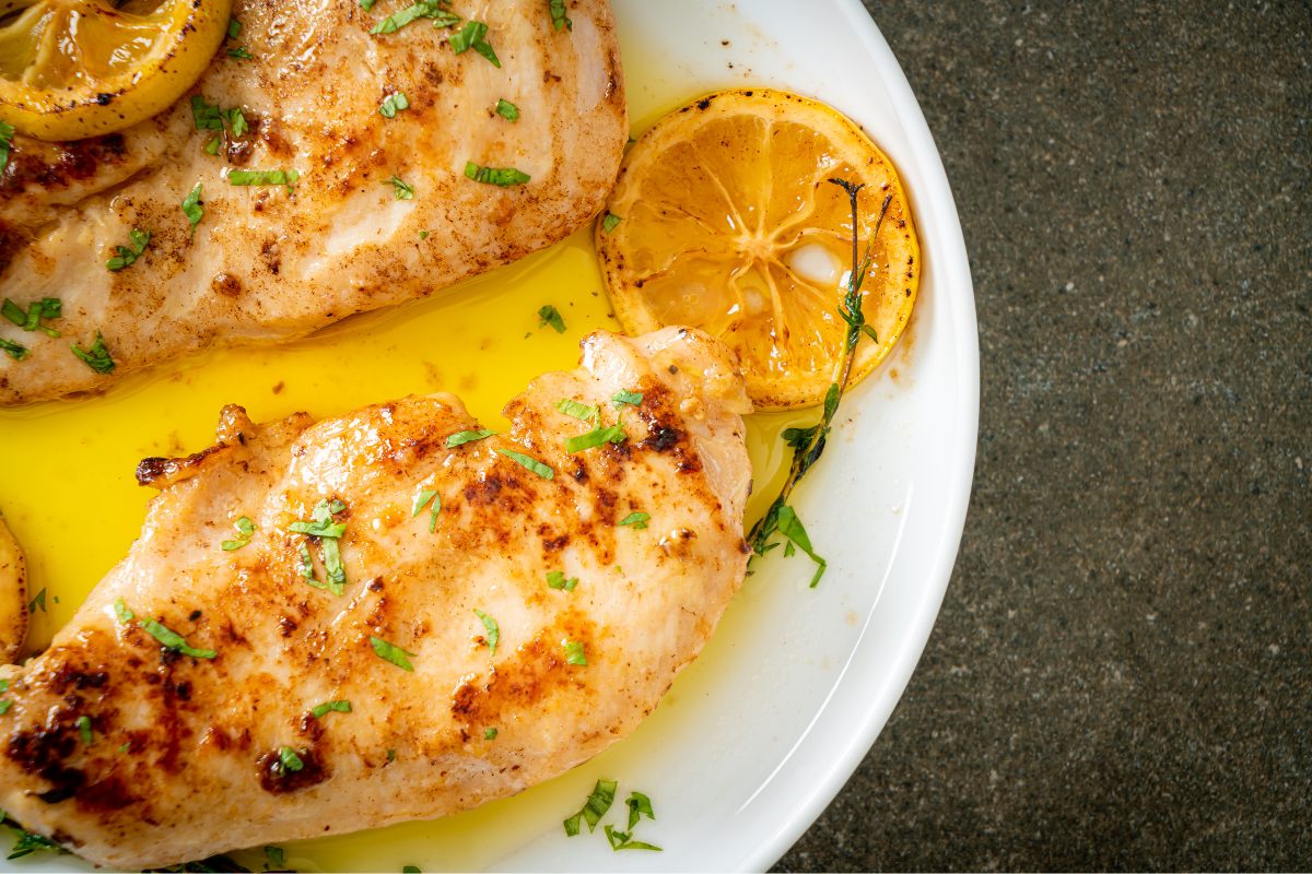 Two baked chicken breats with butter, lemon and garlic, decorated with chopped parsley.