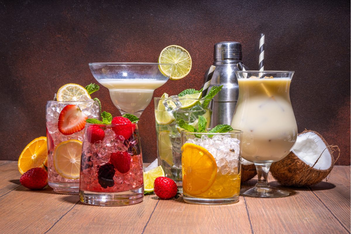 An assortment of colorful mocktails in various glasses, including fruity and creamy beverages, garnished with fresh fruits and mint leaves.