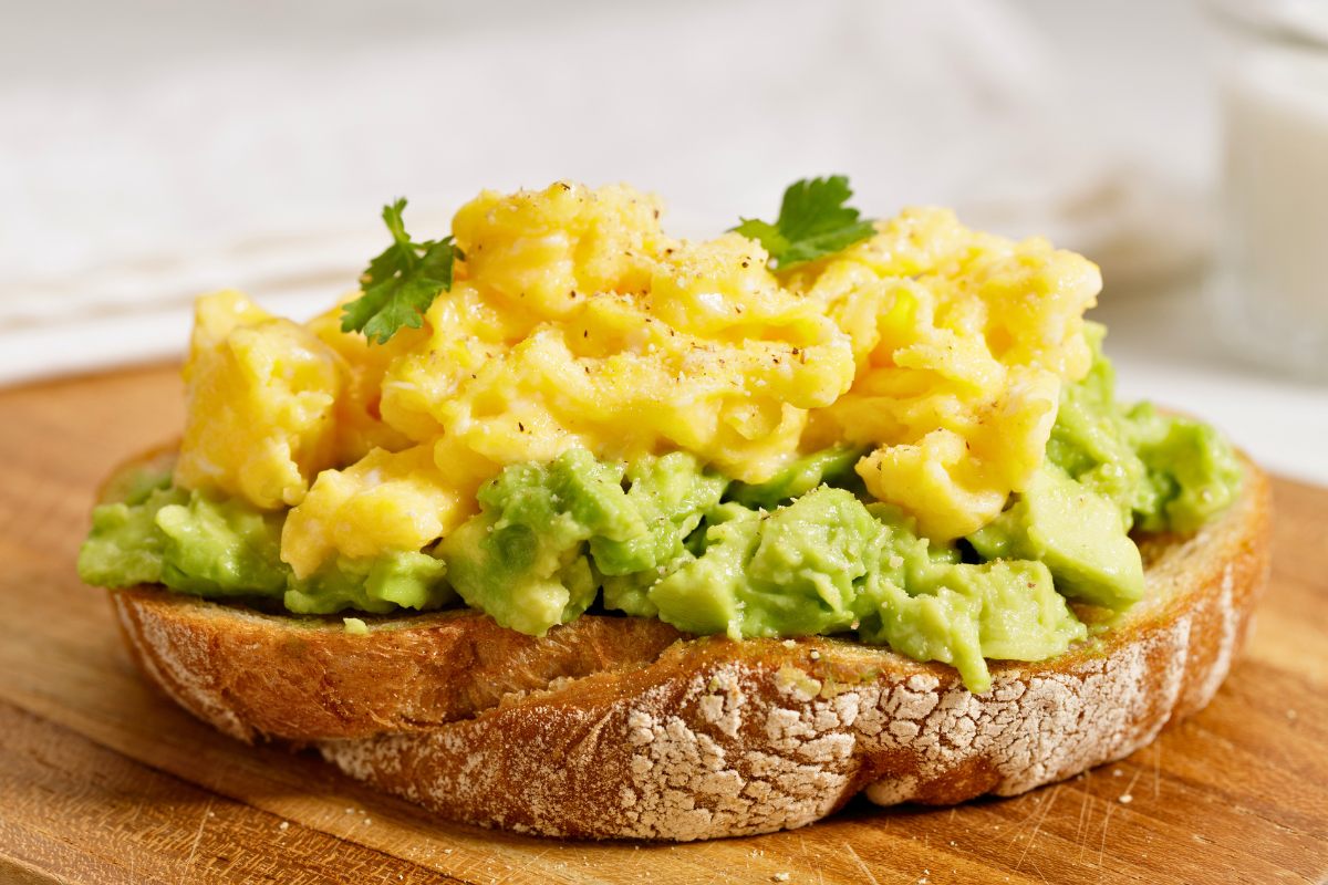 Toast topped with mashed avocado and fluffy scrambled eggs, garnished with fresh herbs.