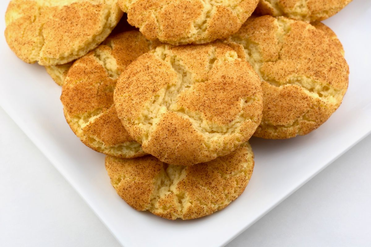 Close-up of a plate of snickerdoodle cookies coated in cinnamon sugar, stacked on a white plate.