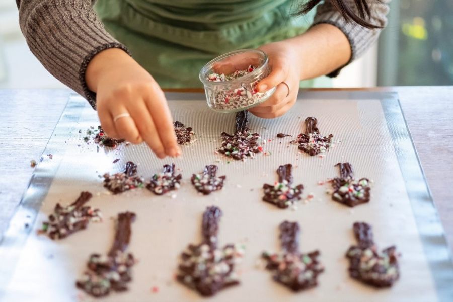 Home baker decorating chocolate Christmas tree shapes with crushed candy cane.