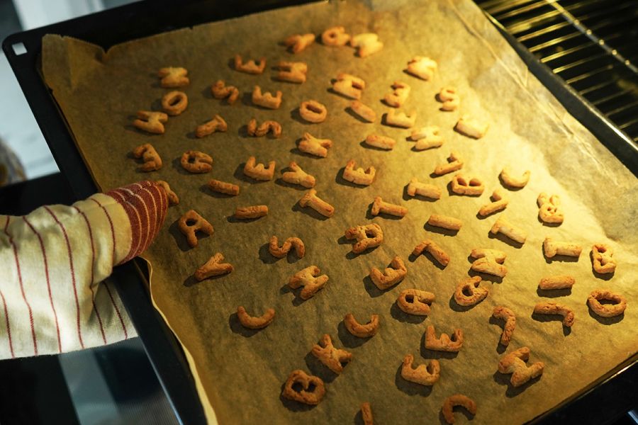 Baking tray with tasty homemade cookies in letters shape taking out from oven.