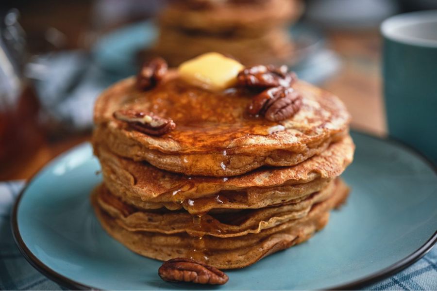 A stack of sweet potato pancakes with a piece of butter and pecans on the top, drizzled with maple syrup or honey.