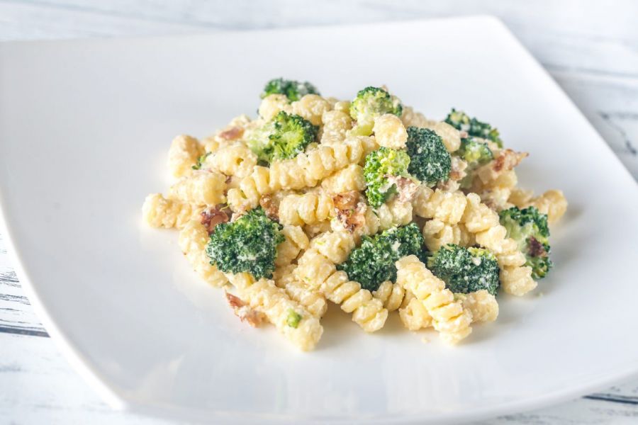Pasta with broccoli, bacon and Alfredo sauce in a square plate.