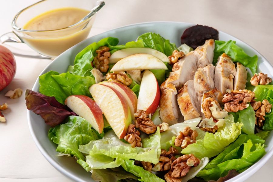 A bowl of chicken, apple and walnut salad with some dressing on the side.
