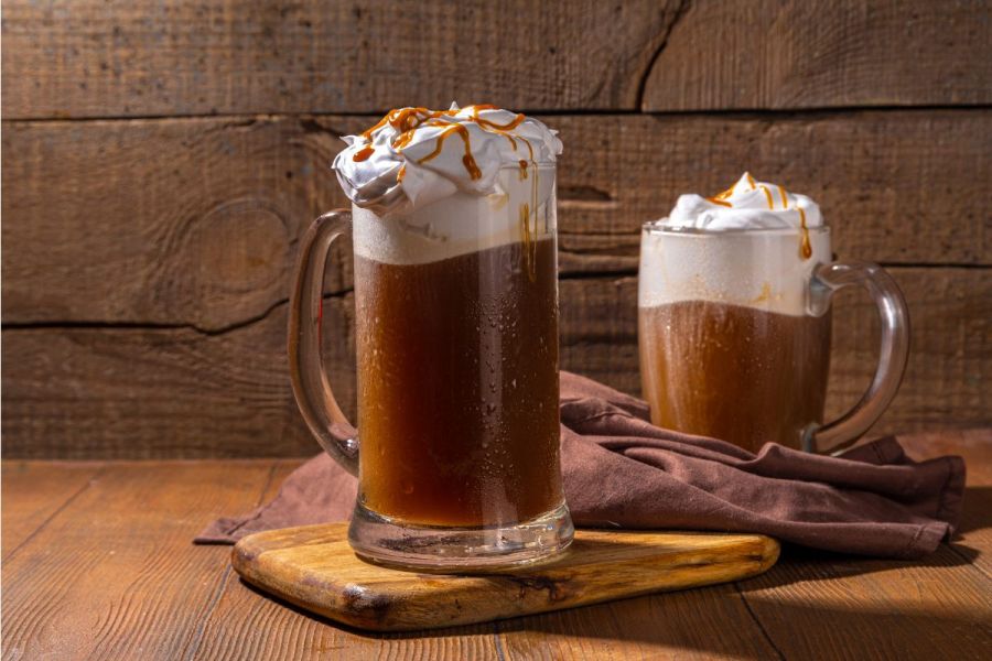 Two large glass mugs filled with homemade butterbeer and topped with whipped cream.