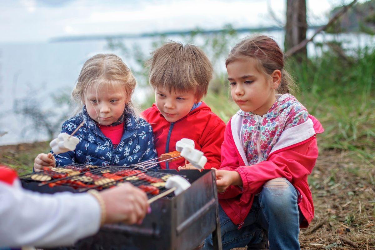 Three children toasting marshmallows at an outdoors camp.