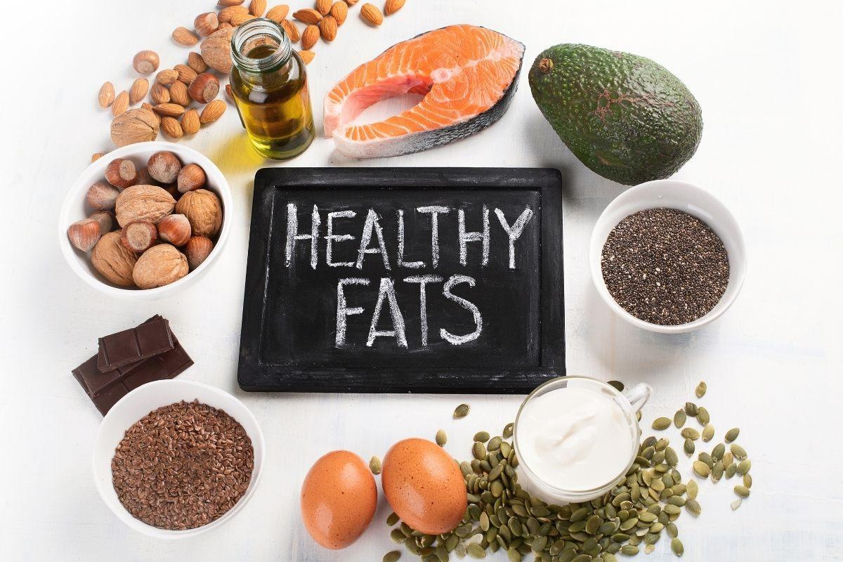 A blackboard with the words healthy fats surrounded by aliments which are source of healthy fats.